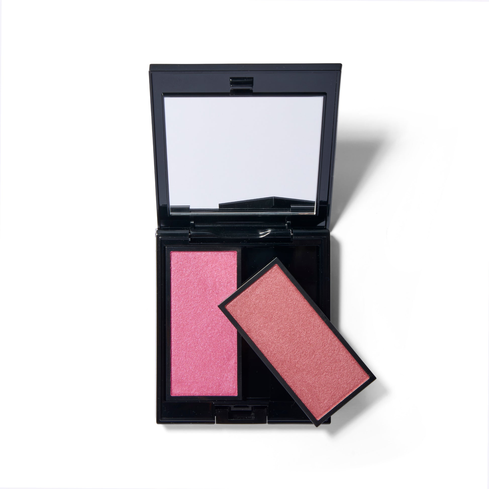 The black Compact Case I, open with the mirror showing. There are two shades of blush in the image, one inserted into the case and one pan of blush is resting on top of the other at an angle showing that the blush pans pop out. 