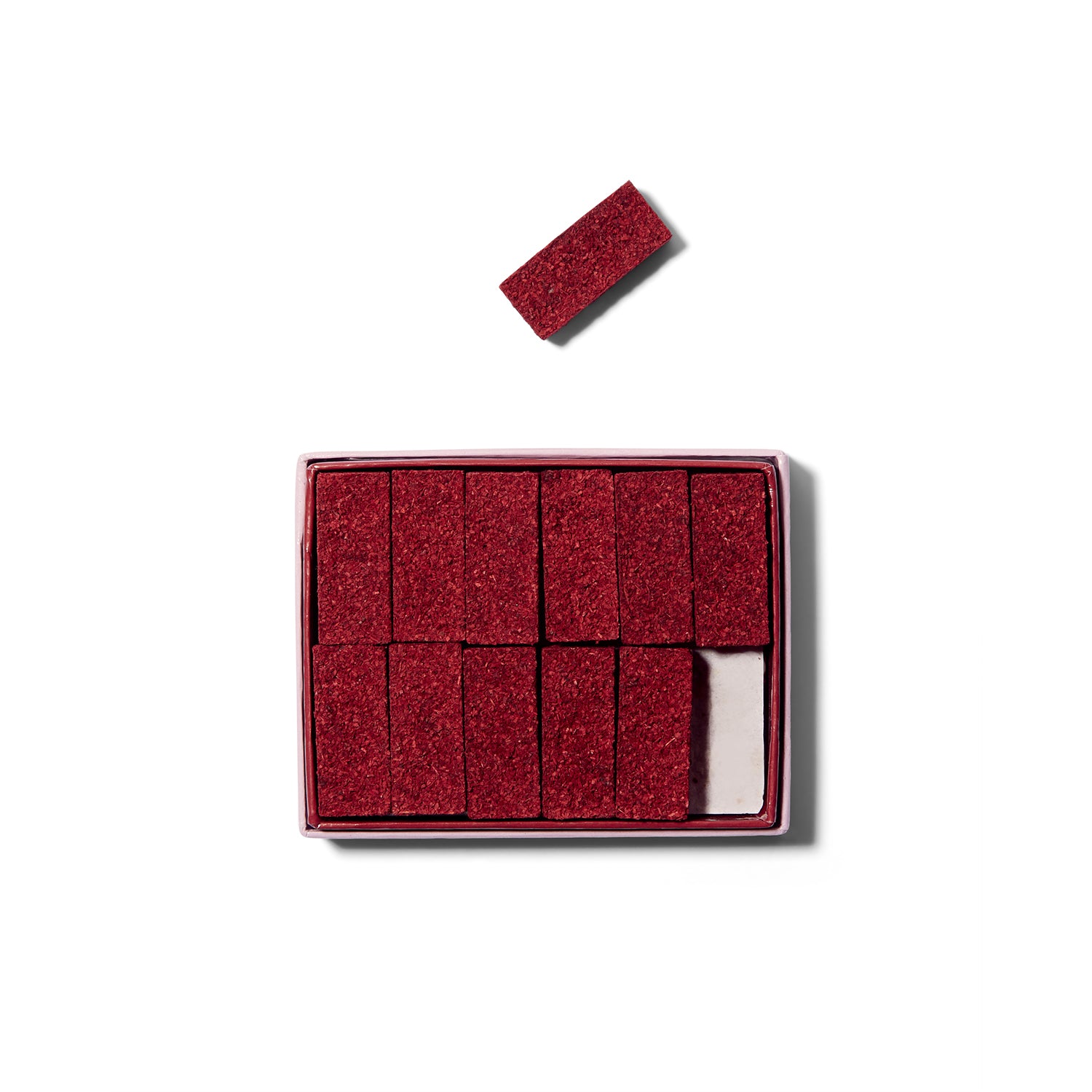 Top view of an open box of Diffusion Rosincrunienne Dat Rosa Mel Apibus incense cubes. 11 cubes are inside the box and one cube is above the box. and the incense is a deep pink.