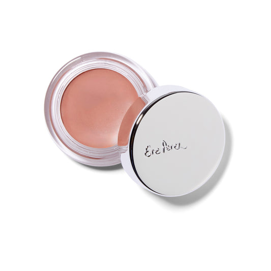 An overhead view of the Ere Perez Carrot Color Pot cream blush. The product is in a squat glass jar with a silver lid. The lid is partially resting on the edge of the glass container. The blush shown is Harmony, a bright orange color.