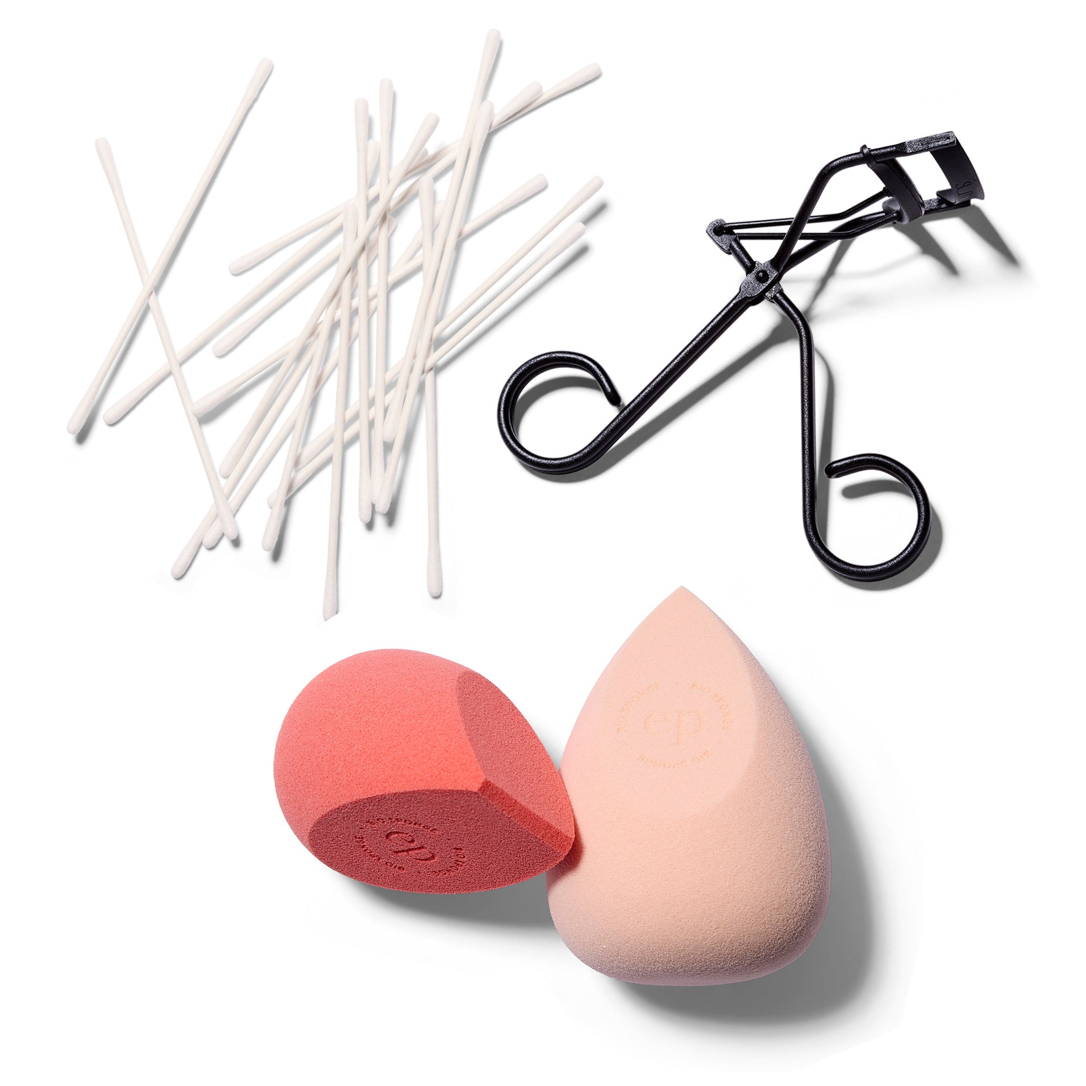 A spray of thin cotton buds, a black eyelash curler and two beauty sponges; one pale peach and on melon pink.