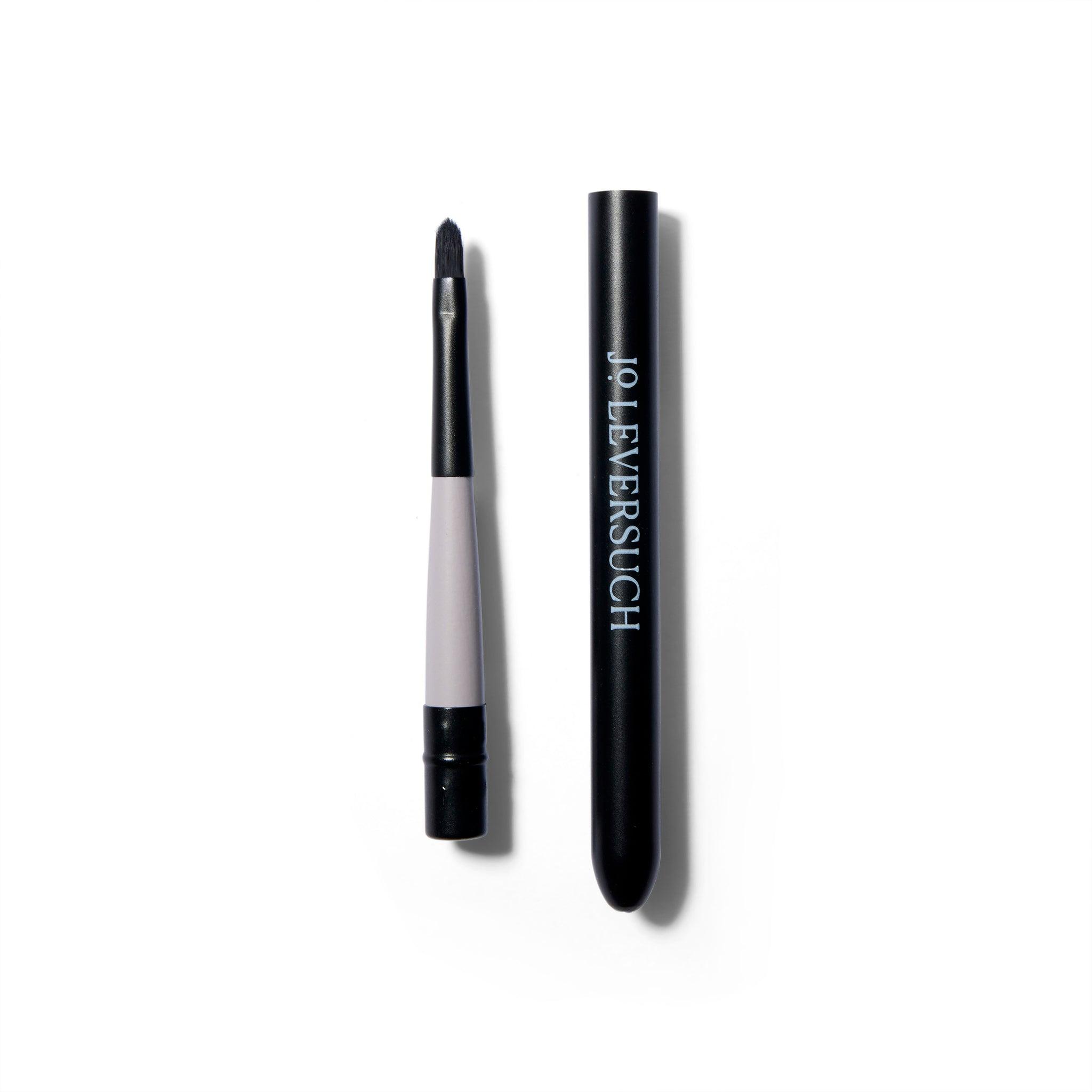 The fine tipped application brush is next to the hollow tube that attaches to the end of the brush. The casing is black with white type.
