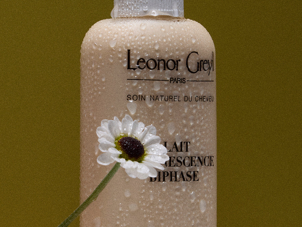 A close up of a bottle with water droplets on it. A white daisy, also with droplets on it, is in front of the left side of the bottle.  