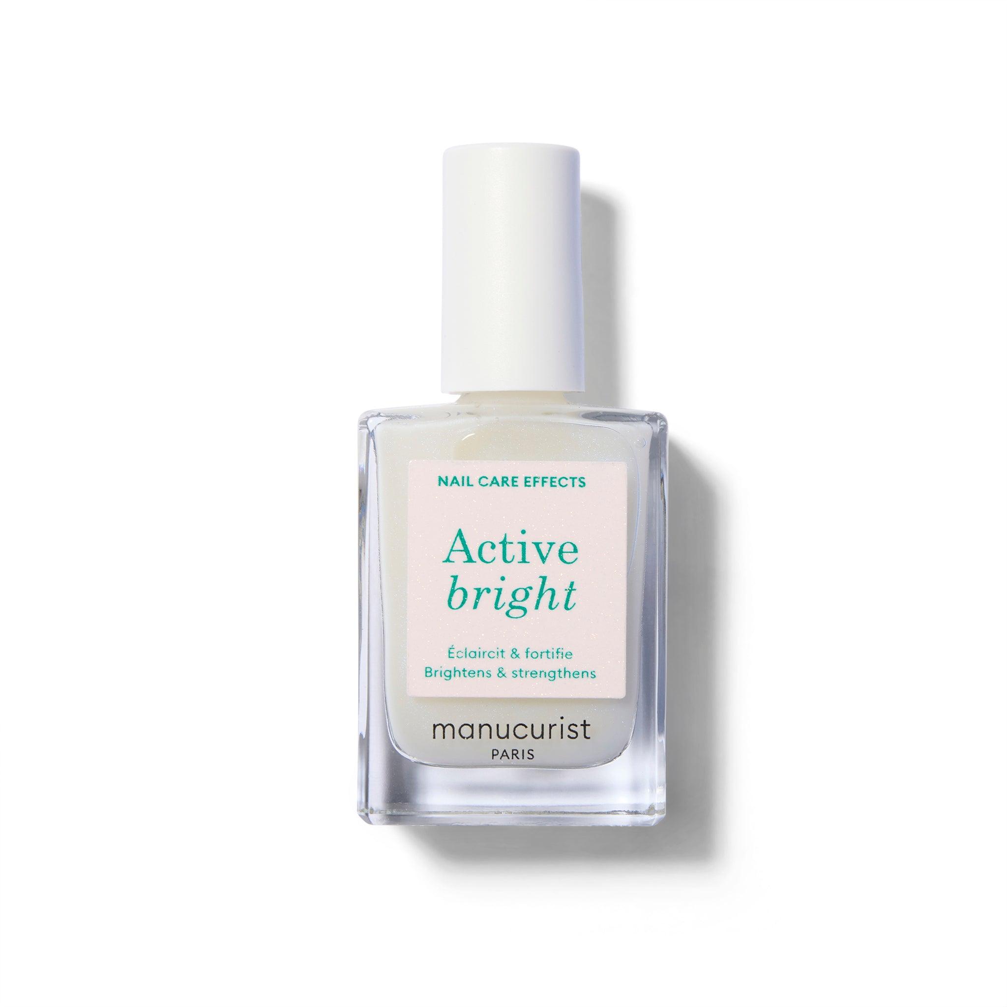 A clear glass nail polish bottle with a sticker with green text. The bottle has a white cap and the polish inside is a cream color with an opal tint.