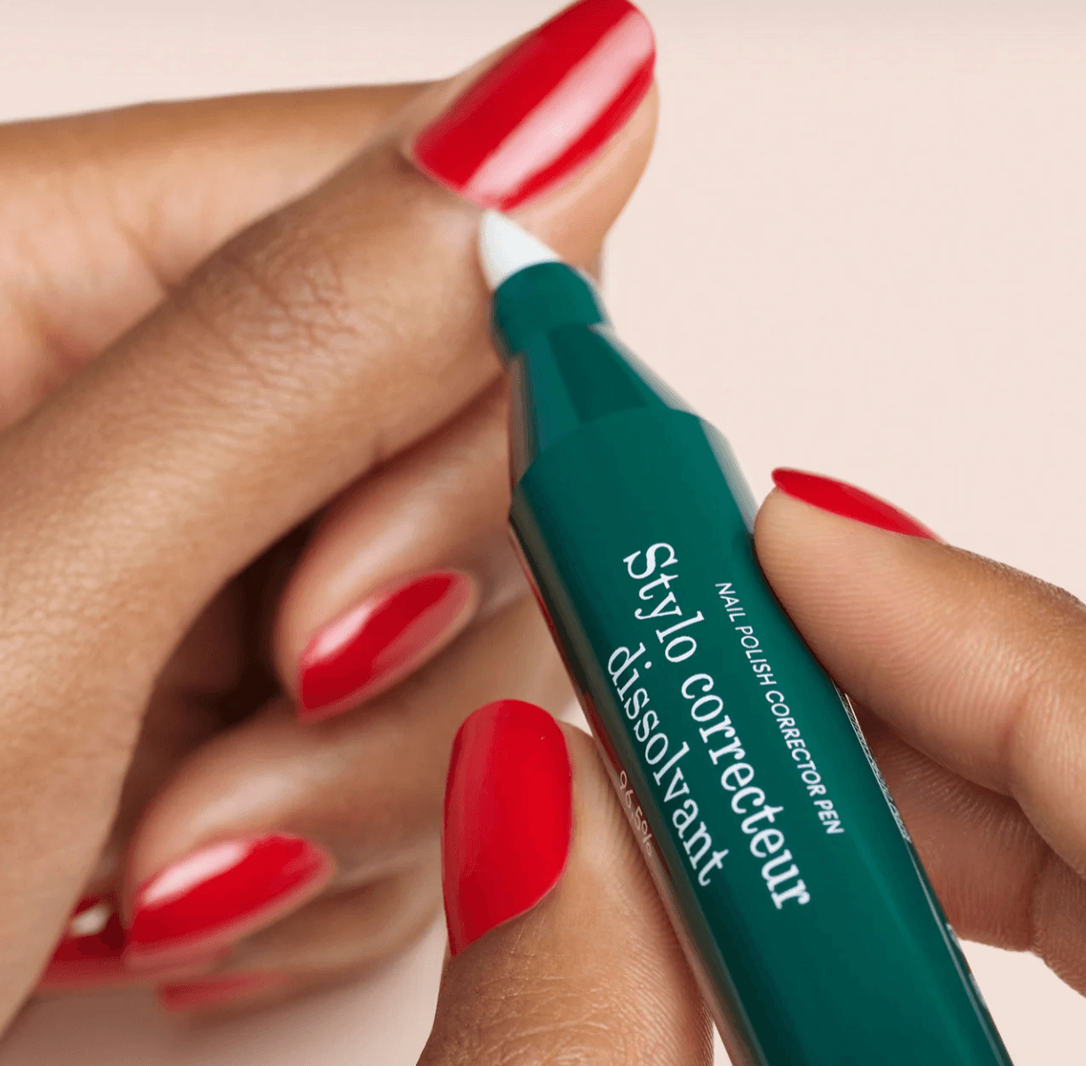 A woman's hands with red nail polish using the product to remove polish from the area around her nails.
