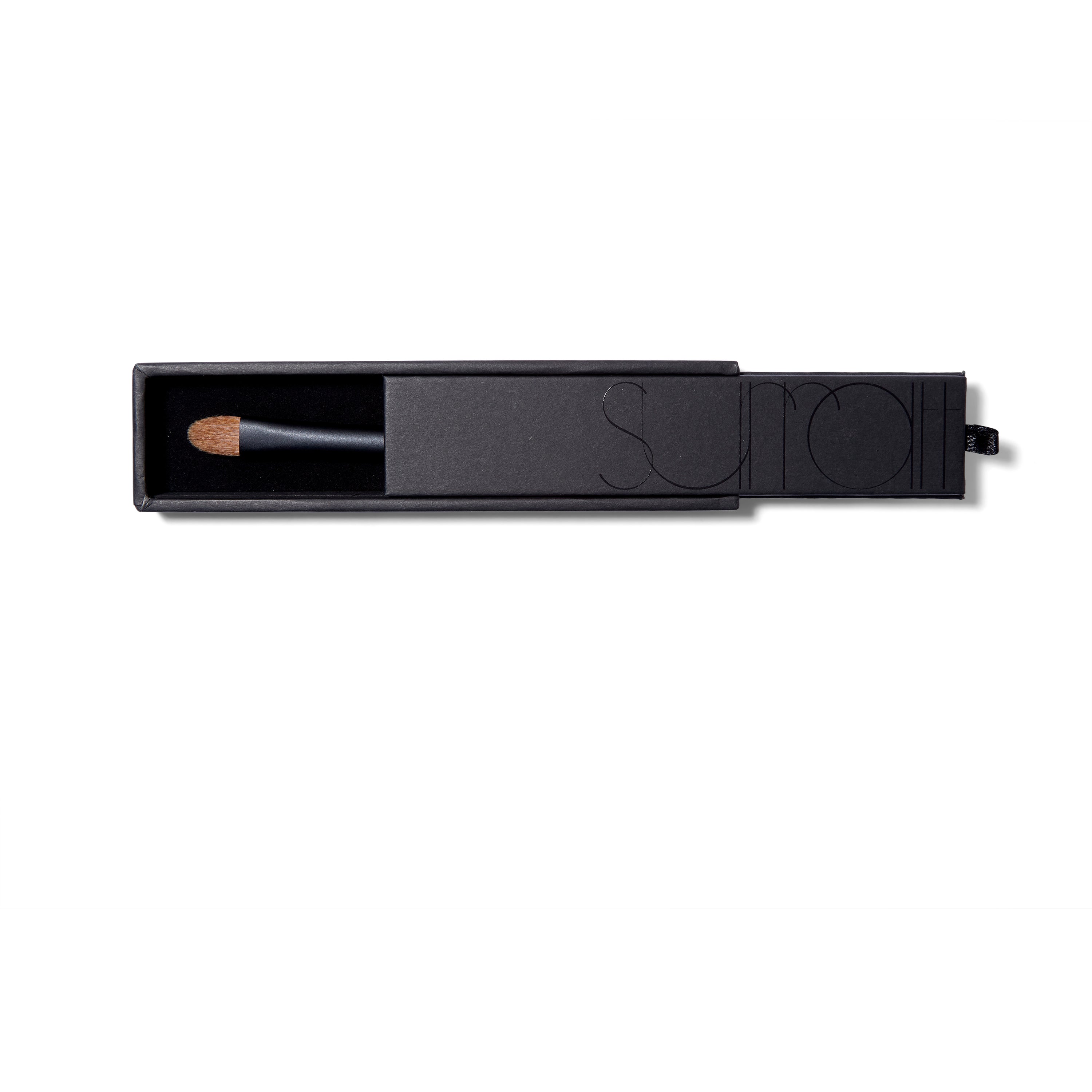 The Surratt Perfectionniste Complexion brush. in a black sturdy box. The handle is black with subtle purple shimmer. The natural bristles are brown and in a soft curved taper.