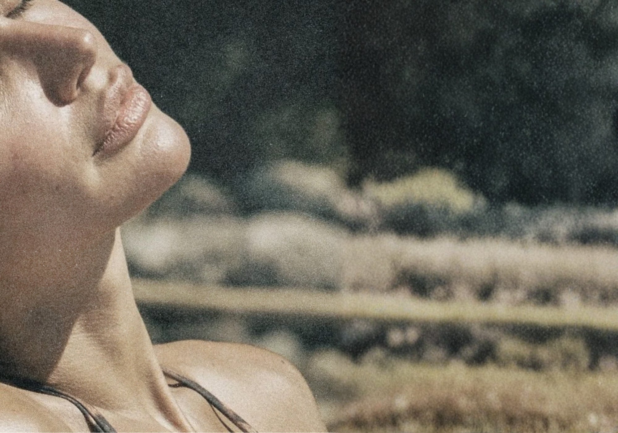 Close-up of a woman's face and neck in an outdoor setting with blurred trees and grass in the background.