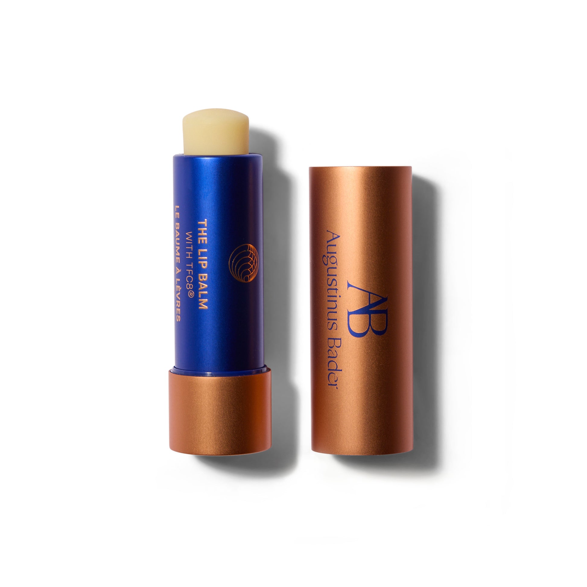 A waxy lip balm stick in a blue and matte  metallic tube. The cap is off and to the right of the lip balm. The lip balm is wound up slightly so you can see the balm bullet.