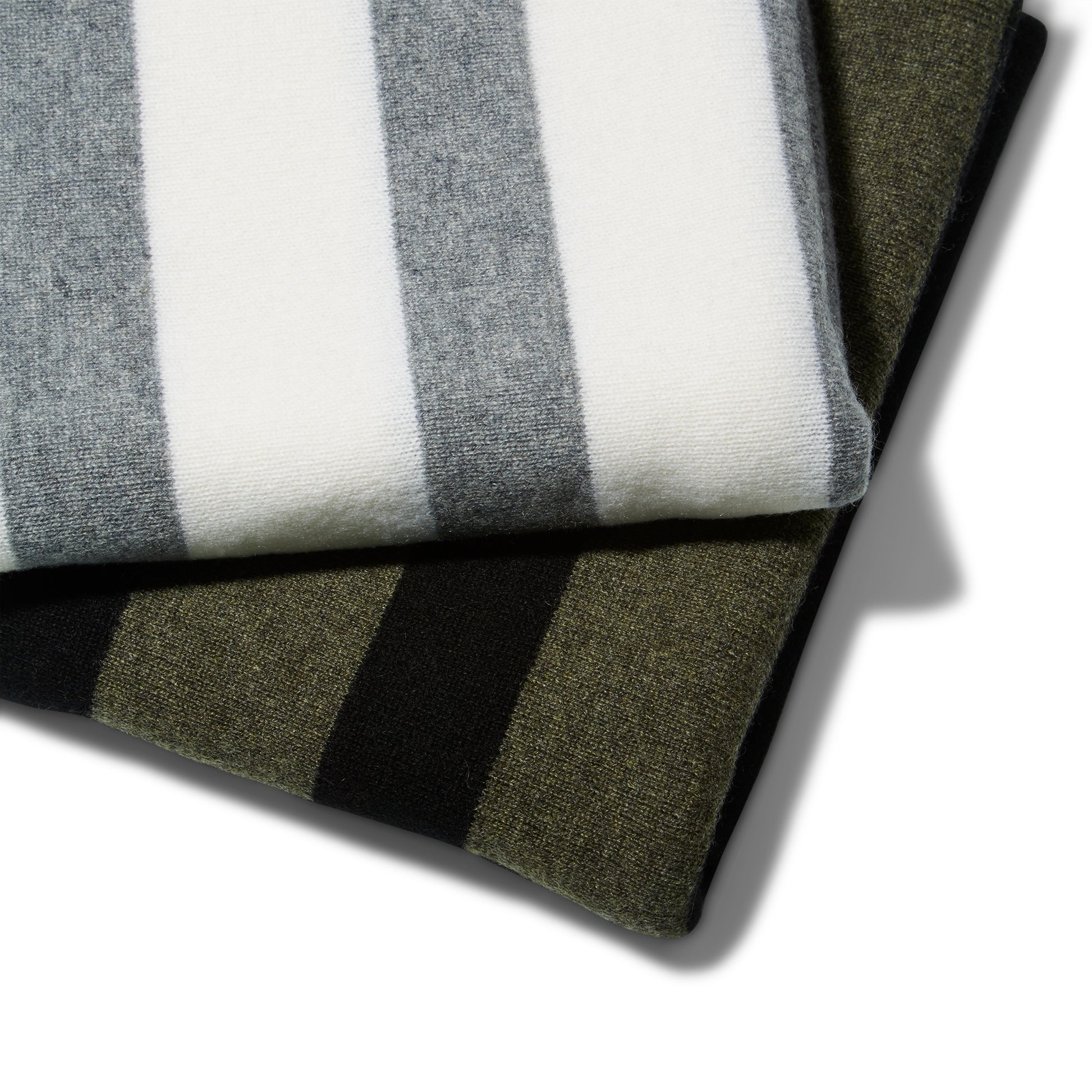 Two Reed Clarke Cashmere Travel blankets. A folded grey blanket with wide white stripes laying partially on top of a black blanket with wide olive green stripes.