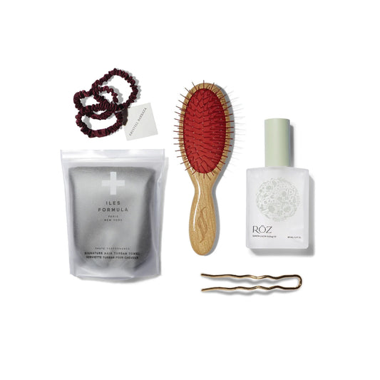 Collection of hair products including the Krystell Barraza Silk Hair Ties in Plum, the Iles Formula Signature Hair Turban Towel in Grey, the Sheila Stotts Wood Handle Untangle Brush, the ROZ Santa Lucia Styling Oil and the Reed Clarke 4" 22k gold plated hair pin.