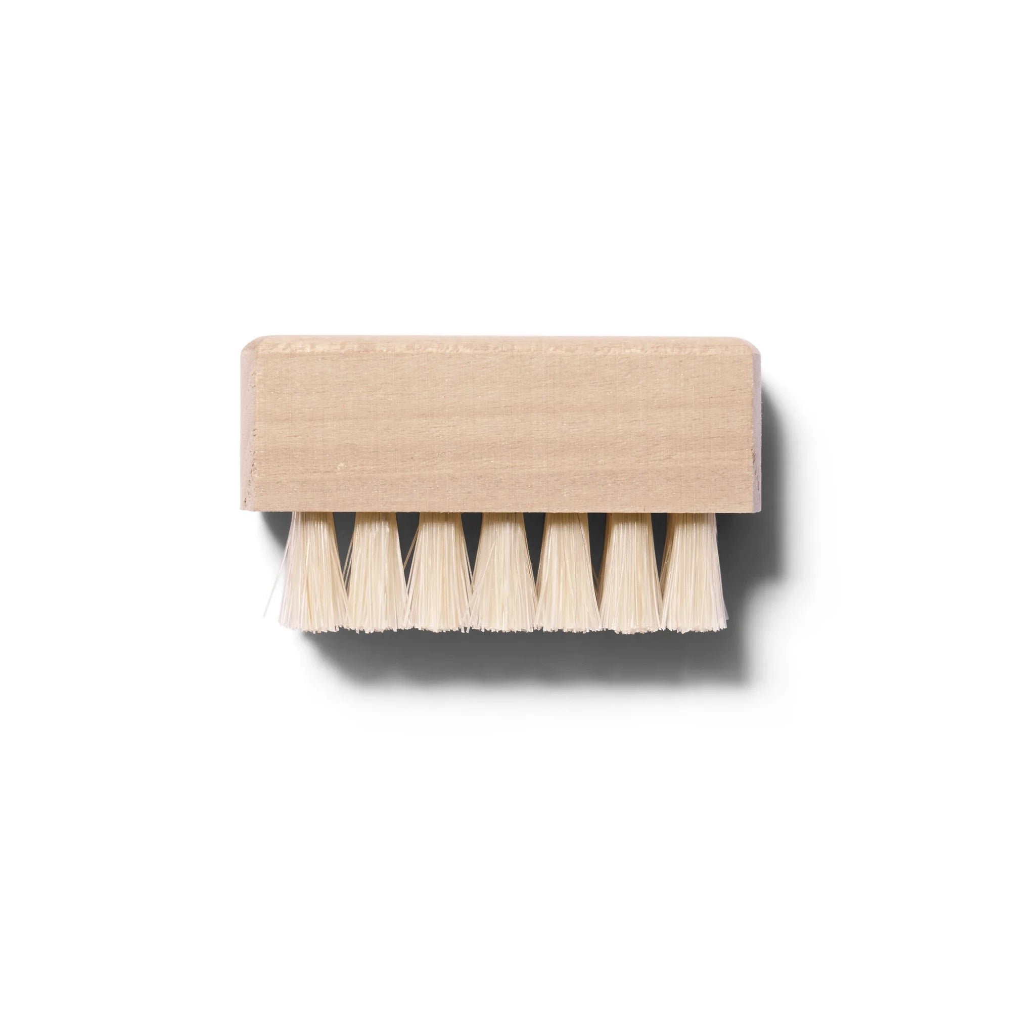 Small light colored wooden nail brush with natural hair bristles photographed from the side. 