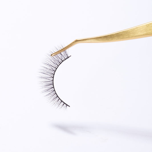 Side close up view of the gold Kasha Eyelash Applicator. The applicator is gold and the tip is angled. The applicator is holding a strip lash.