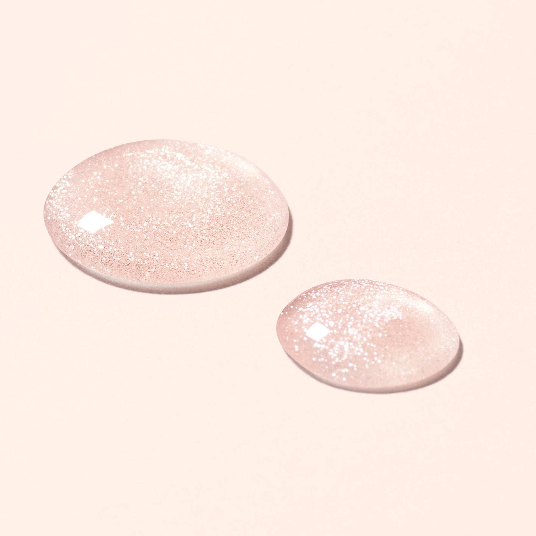 Two dollops of the Active Shine nail polish - a sheer being with shimmer -  on a light peach background.
