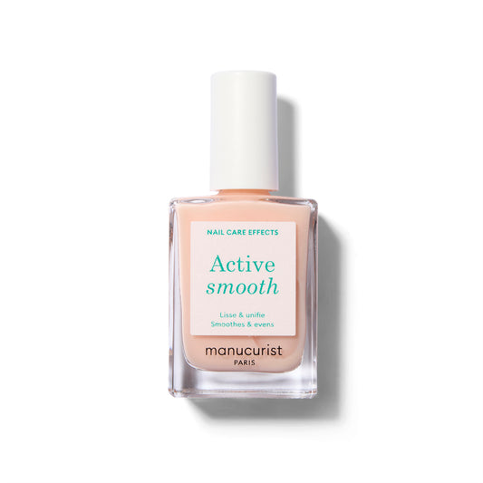 A clear glass nail polish bottle with a white label with green text. The polish is a sheer, soft peach color.