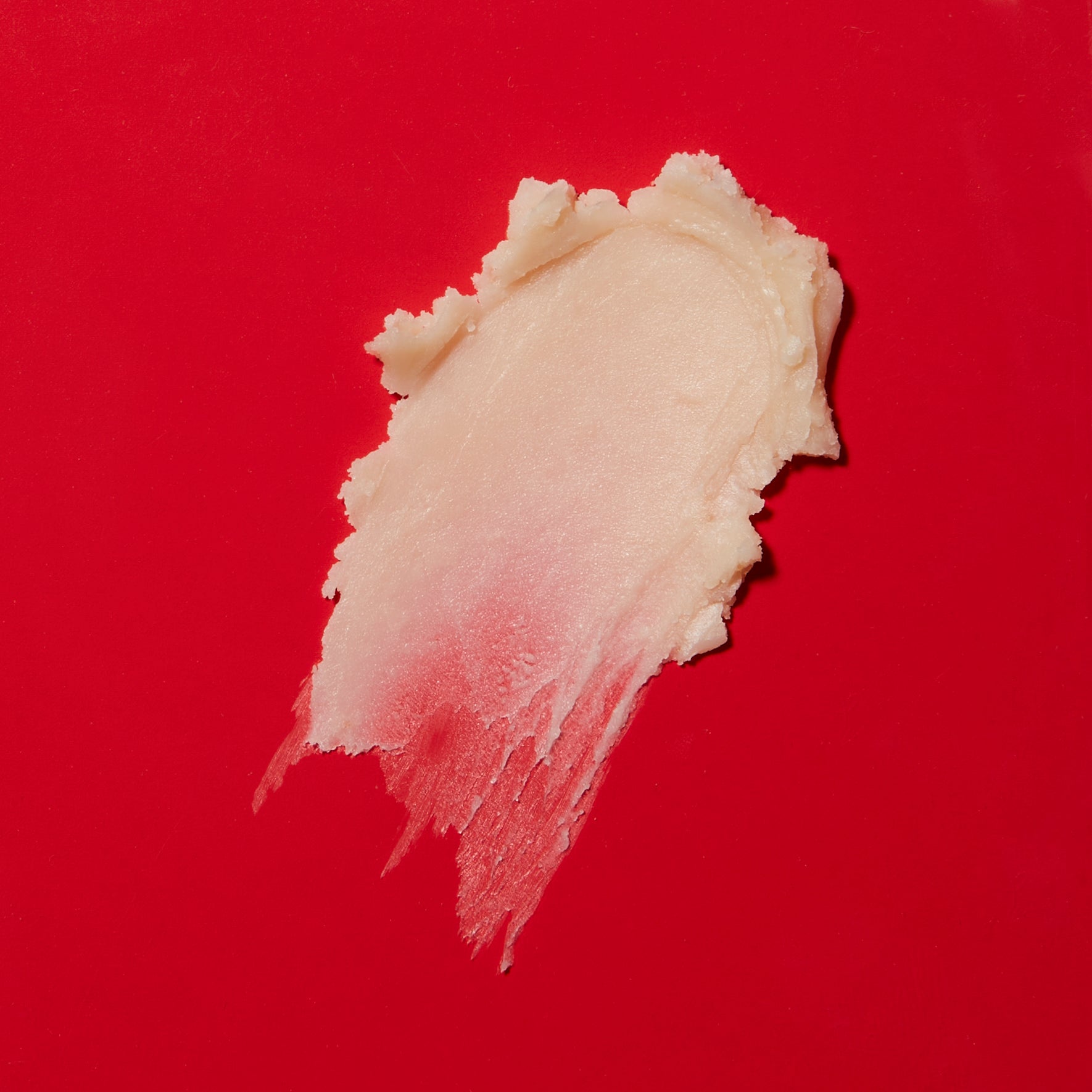 A swatch of the Proshine Solid Body Oil. The swatch of the creamy off white product is on a bright red background.