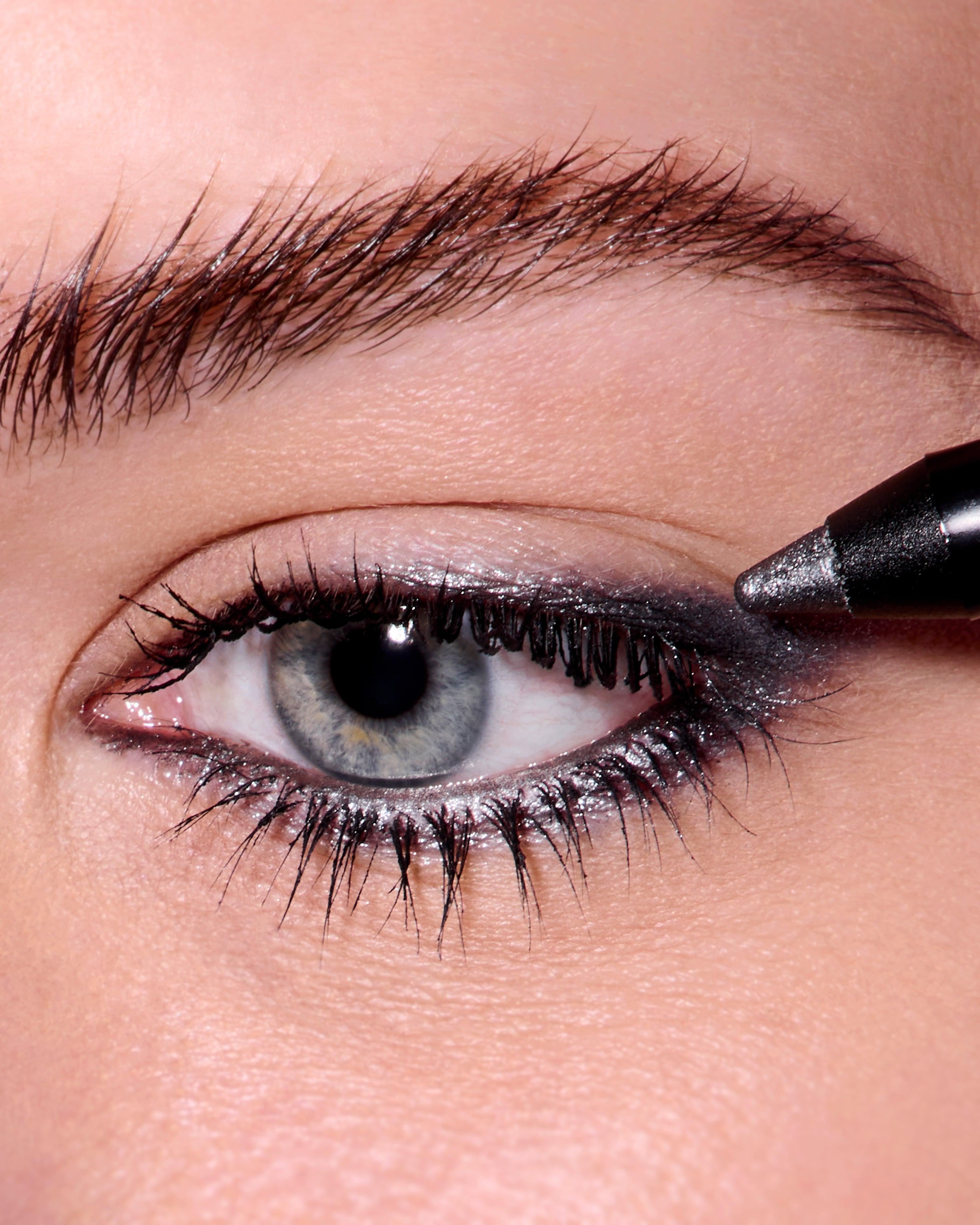 Close up of a woman's eye. Her skin is fair and her eyes are blue. Her eyes are rimmed in the Roen Eyeline Define Shimmering Gunmetal and the pencil is touching the out edge of her eye, applying the liner. 