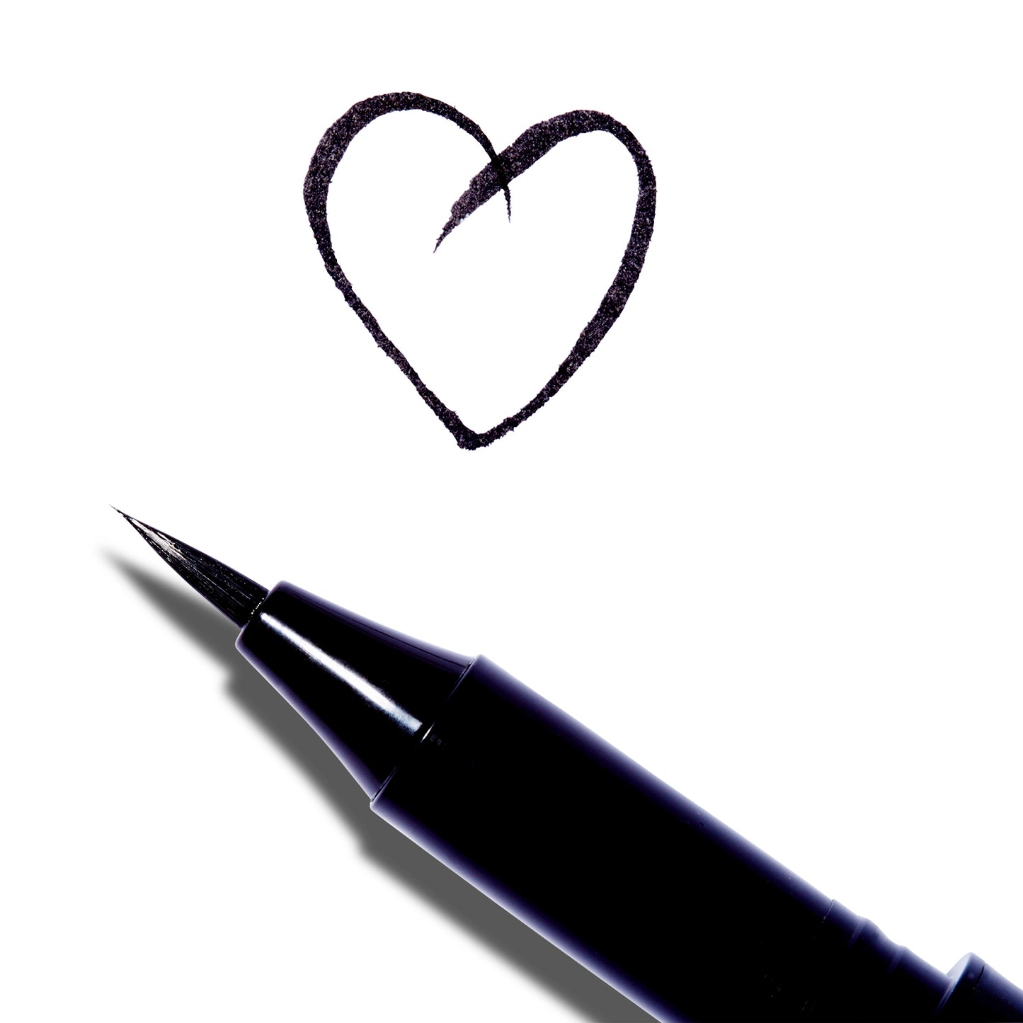  A close up of the Surratt Autographique Liquid Eyeliner in Chat Noir, a deep black. The pen is made of individual hairs and goes to a sharp point. The pen is angled and there is a heart drawn above it in the ink from the eyeliner.
