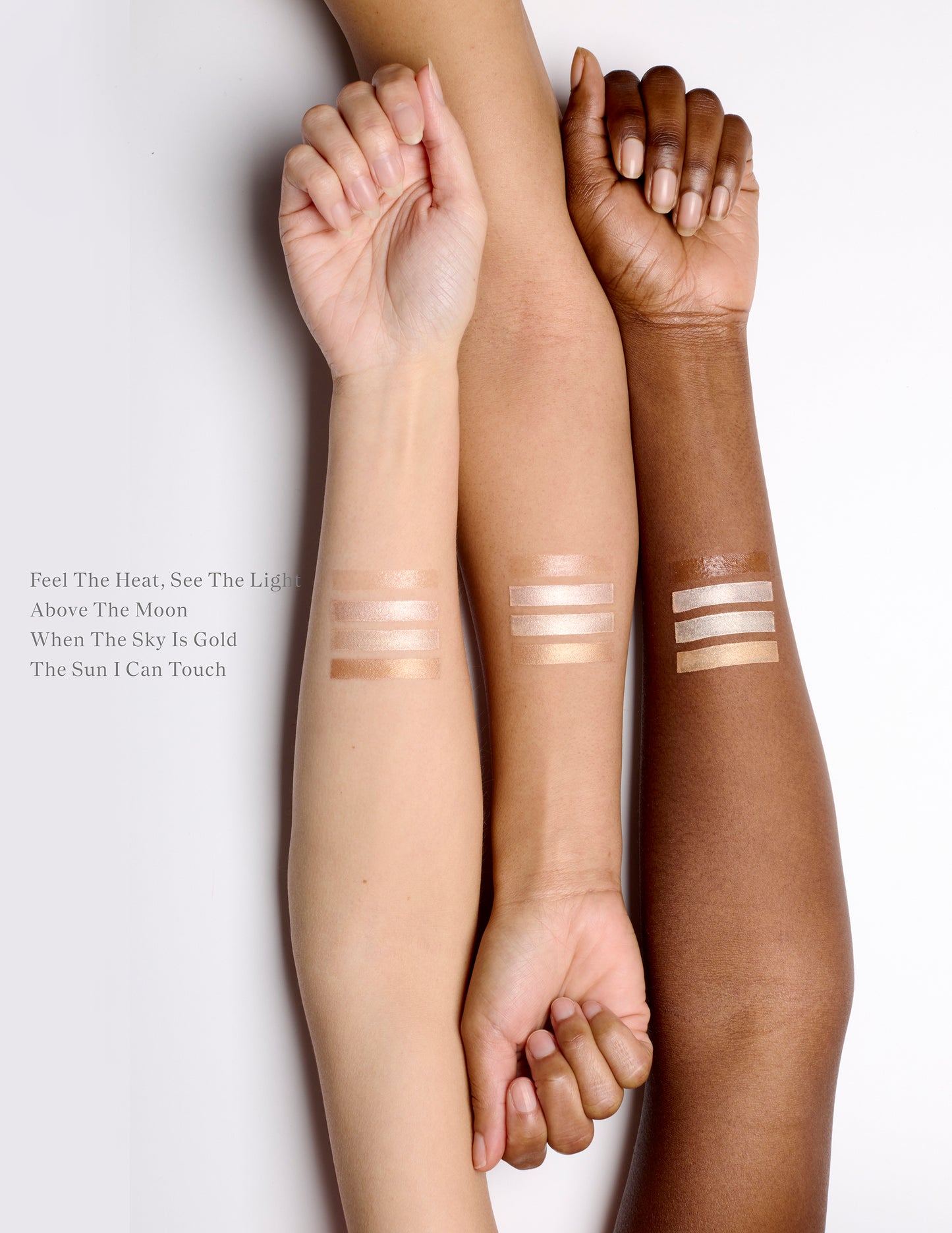 Three arms lined up next to each other with cream highlighter swatches on the skin.  There are four swatch stripes on each of the three arms. The arm on the left is fair, the middle is golden and the arm on the right is deep. Their nails are unpainted and their hands are semi-closed in a relaxed state.